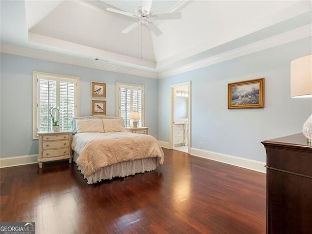 bedroom with dark wood-type flooring, ornamental molding, connected bathroom, and a tray ceiling