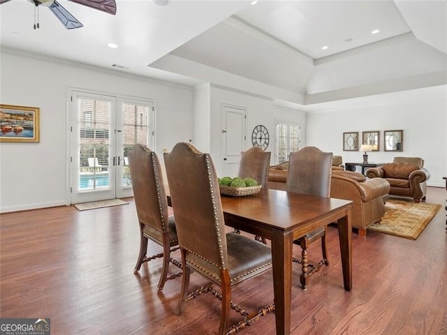 dining room featuring a raised ceiling, wood-type flooring, and a healthy amount of sunlight