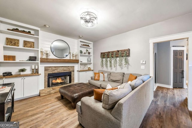 living room featuring built in features, a stone fireplace, and light hardwood / wood-style flooring