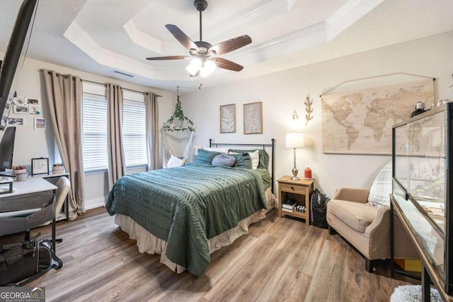 bedroom with a raised ceiling, light wood-type flooring, and ornamental molding