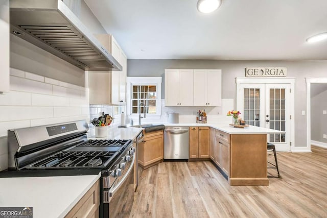 kitchen with french doors, kitchen peninsula, appliances with stainless steel finishes, a kitchen bar, and wall chimney exhaust hood