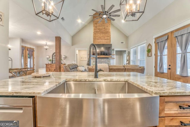 kitchen featuring ceiling fan with notable chandelier, sink, hanging light fixtures, light stone counters, and french doors