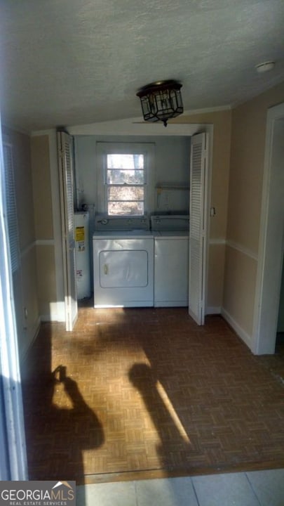 laundry area with water heater, dark parquet flooring, a textured ceiling, and washing machine and dryer