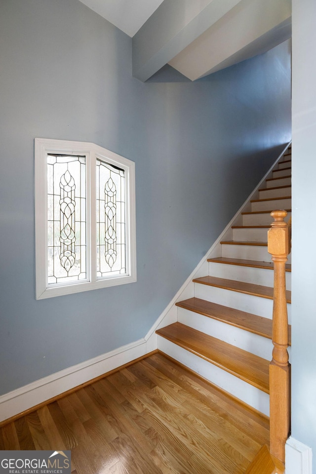 stairway with hardwood / wood-style floors and beamed ceiling