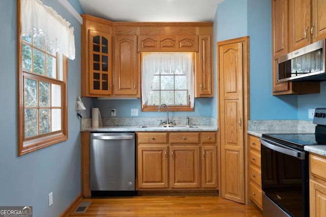 kitchen with sink, light wood-type flooring, light stone countertops, and appliances with stainless steel finishes