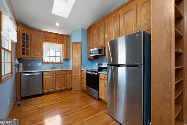 kitchen featuring lofted ceiling with skylight, appliances with stainless steel finishes, sink, light stone countertops, and light wood-type flooring