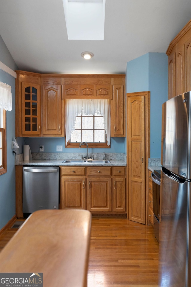 kitchen featuring appliances with stainless steel finishes, sink, light wood-type flooring, and a skylight