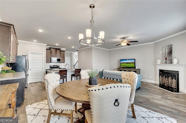 dining space featuring crown molding, sink, ceiling fan with notable chandelier, and light wood-type flooring