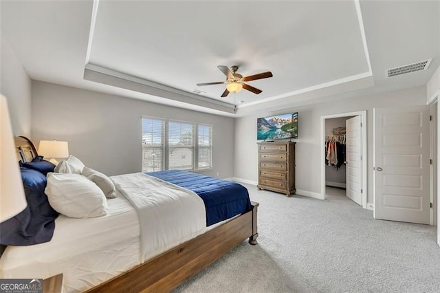 bedroom with ceiling fan, light colored carpet, a tray ceiling, and a spacious closet