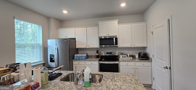 kitchen with stainless steel appliances, white cabinetry, sink, and light stone counters