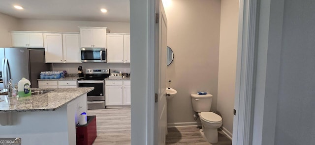 kitchen featuring white cabinetry, stainless steel appliances, light stone counters, and light wood-type flooring