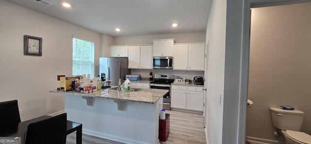 kitchen featuring sink, appliances with stainless steel finishes, white cabinetry, a kitchen breakfast bar, and light stone countertops