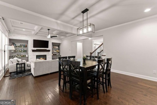 dining area with dark wood-type flooring, coffered ceiling, ornamental molding, a stone fireplace, and beamed ceiling