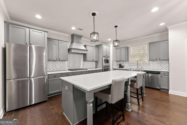 kitchen with premium range hood, appliances with stainless steel finishes, decorative light fixtures, a center island, and dark wood-type flooring