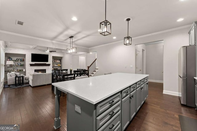 kitchen with a stone fireplace, a center island, pendant lighting, and stainless steel refrigerator