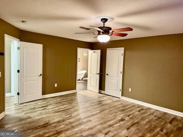 unfurnished bedroom featuring ceiling fan, ensuite bathroom, light hardwood / wood-style floors, and a textured ceiling