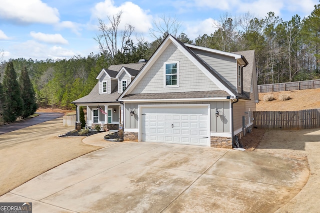 view of front of home featuring concrete driveway, board and batten siding, stone siding, and fence