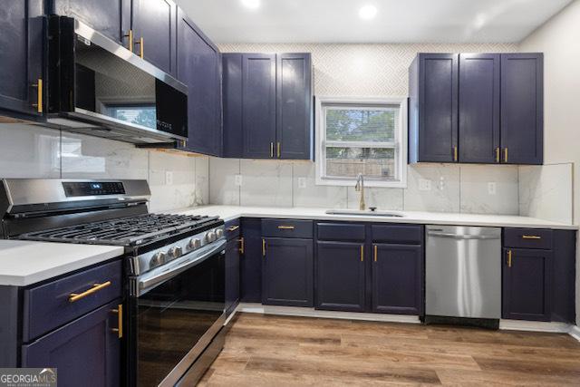 kitchen with tasteful backsplash, stainless steel appliances, sink, and light wood-type flooring