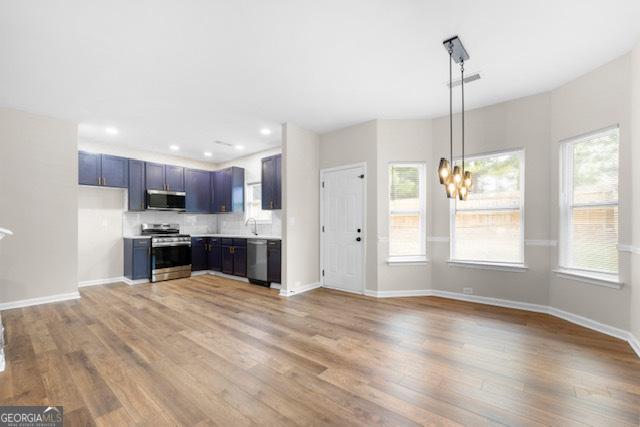 kitchen featuring an inviting chandelier, stainless steel appliances, light hardwood / wood-style floors, decorative backsplash, and decorative light fixtures