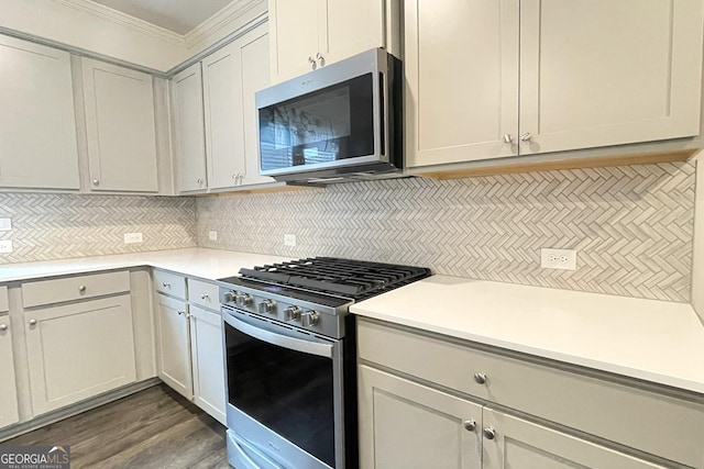 kitchen with crown molding, appliances with stainless steel finishes, dark hardwood / wood-style flooring, and backsplash