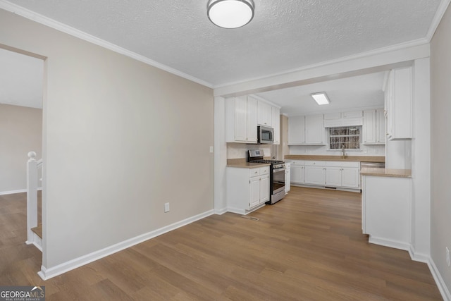 kitchen with white cabinetry, ornamental molding, appliances with stainless steel finishes, and light hardwood / wood-style floors