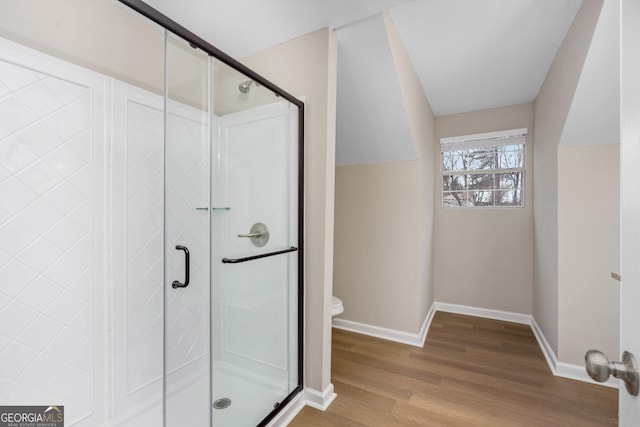 bathroom featuring lofted ceiling, hardwood / wood-style flooring, a shower with door, and toilet