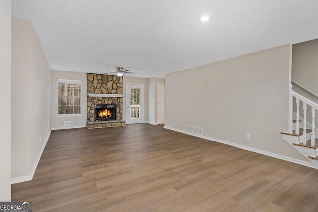 unfurnished living room with hardwood / wood-style flooring, a stone fireplace, and ceiling fan