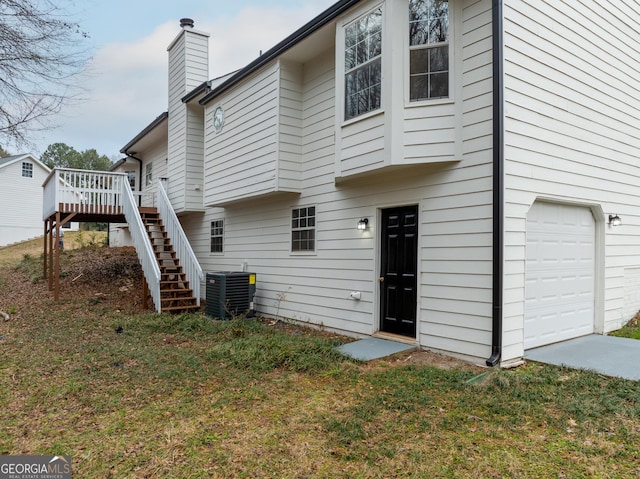 rear view of house featuring a garage, a wooden deck, a yard, and central AC