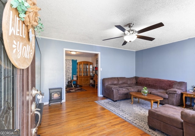 living room with crown molding, a textured ceiling, a wood stove, ceiling fan, and light hardwood / wood-style floors