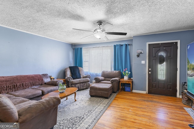 living room featuring ceiling fan, ornamental molding, wood-type flooring, and a textured ceiling