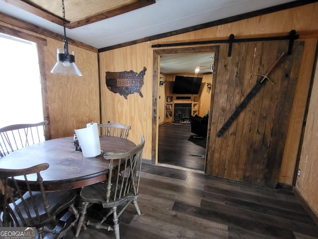 dining room with a barn door, plenty of natural light, dark hardwood / wood-style flooring, and wood walls