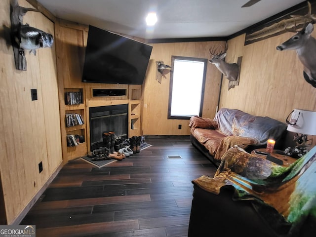 living room with dark wood-type flooring, wooden walls, and a fireplace