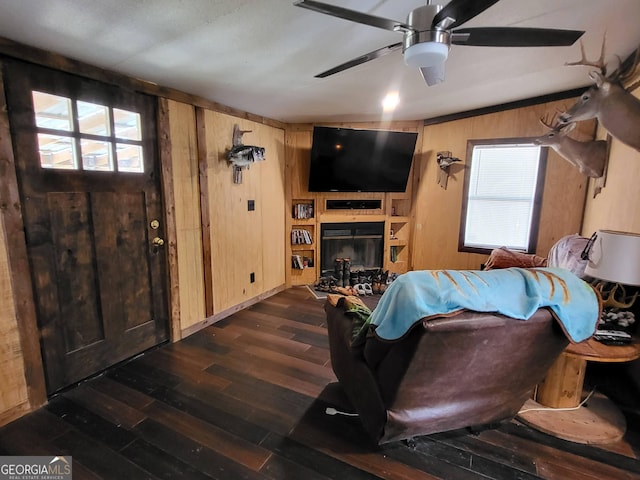 living room with dark hardwood / wood-style floors, ceiling fan, and wood walls