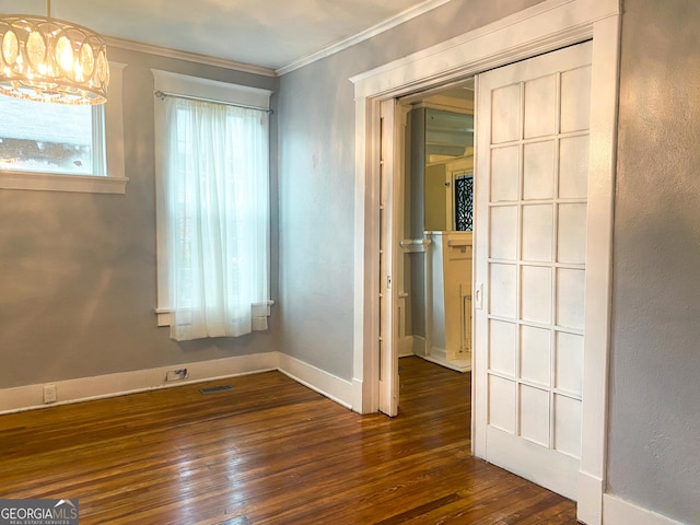 empty room with dark wood-type flooring, crown molding, and a chandelier