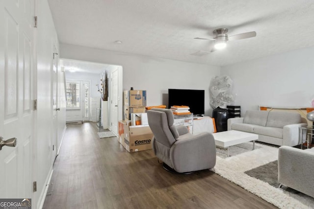 living room featuring dark wood-type flooring, ceiling fan, and a textured ceiling