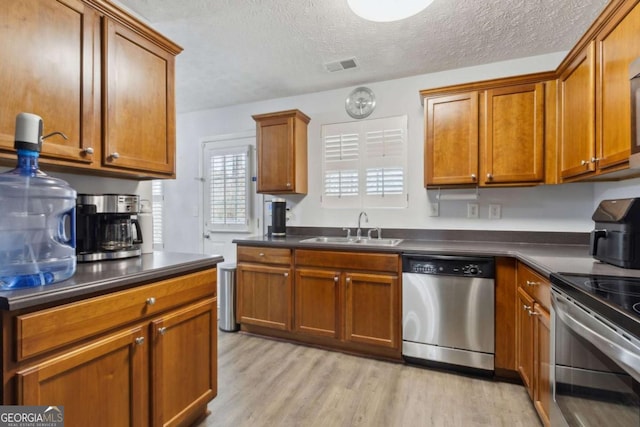 kitchen featuring sink, stainless steel appliances, light hardwood / wood-style floors, and a textured ceiling