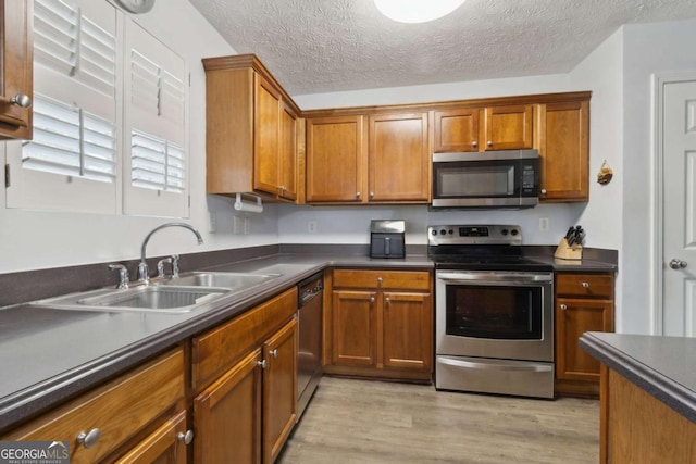 kitchen featuring sink, stainless steel appliances, light hardwood / wood-style floors, and a textured ceiling