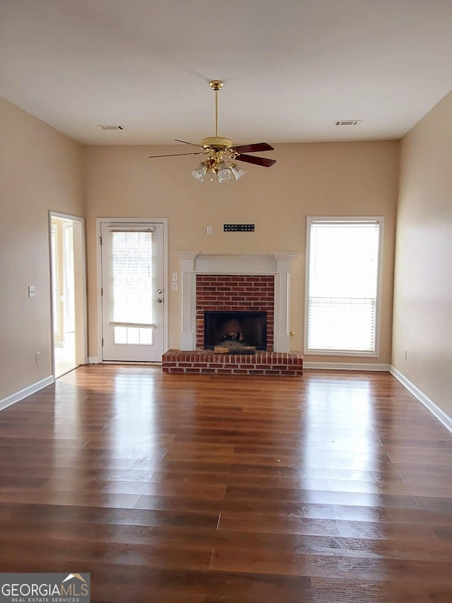 unfurnished living room with a fireplace, visible vents, dark wood finished floors, and a ceiling fan