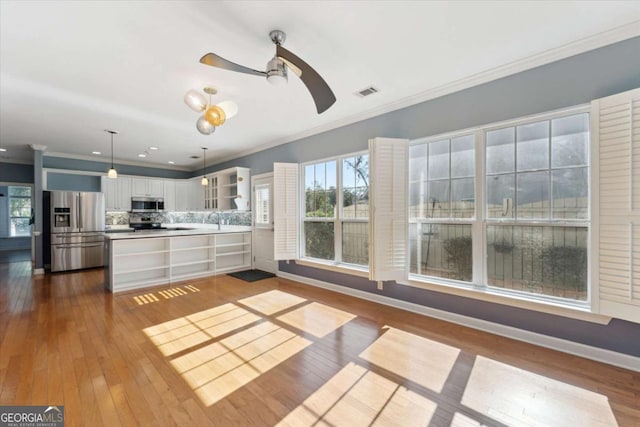 kitchen featuring stainless steel appliances, ornamental molding, hanging light fixtures, and white cabinets