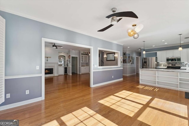 unfurnished living room featuring crown molding, ceiling fan, and light wood-type flooring