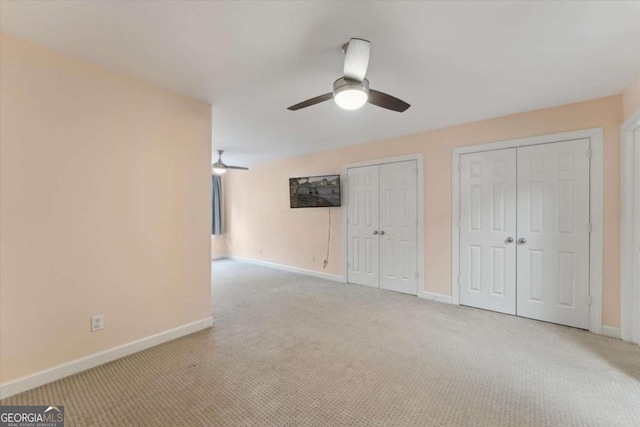 unfurnished bedroom featuring ceiling fan, light colored carpet, and multiple closets