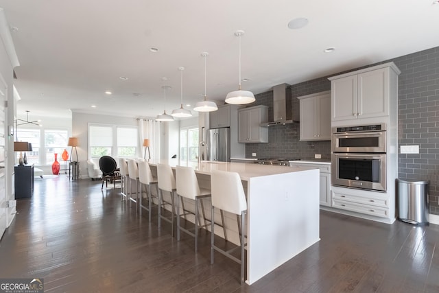 kitchen with a spacious island, a breakfast bar, decorative light fixtures, stainless steel appliances, and wall chimney range hood