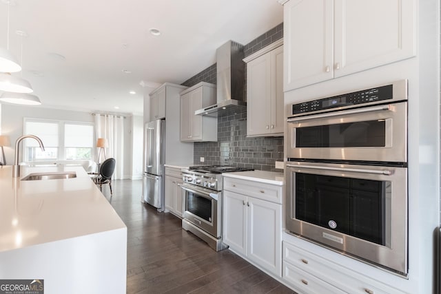 kitchen featuring sink, hanging light fixtures, premium appliances, decorative backsplash, and wall chimney exhaust hood