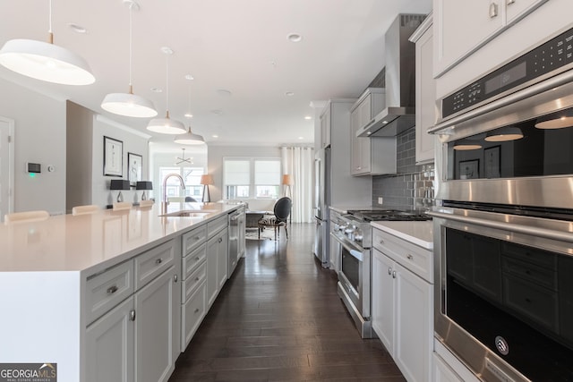 kitchen featuring sink, appliances with stainless steel finishes, pendant lighting, a kitchen island with sink, and wall chimney range hood