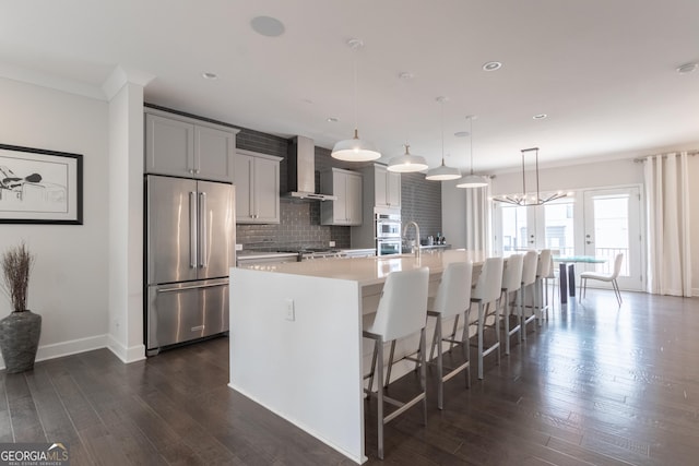 kitchen featuring appliances with stainless steel finishes, a kitchen breakfast bar, pendant lighting, a large island, and wall chimney range hood