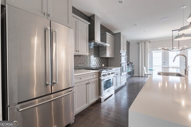 kitchen with decorative light fixtures, tasteful backsplash, sink, high end appliances, and wall chimney range hood