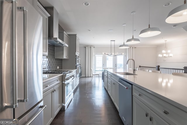 kitchen featuring sink, hanging light fixtures, high end appliances, an inviting chandelier, and wall chimney exhaust hood