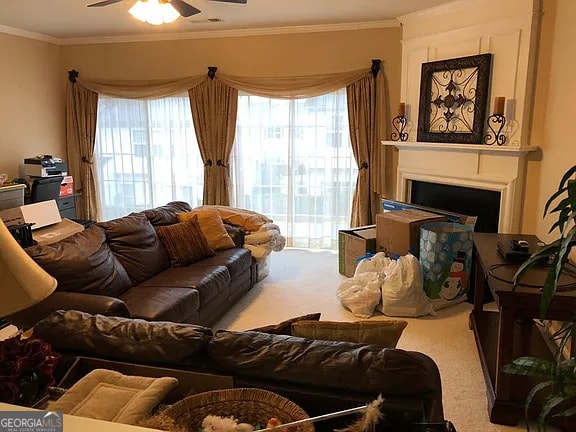 carpeted living room featuring crown molding, a fireplace, and ceiling fan