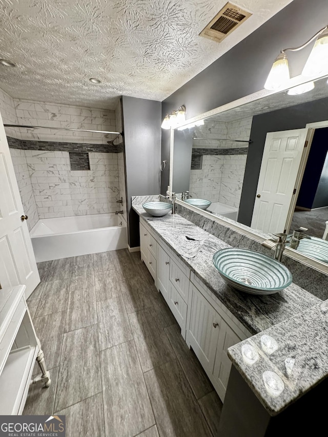 bathroom with vanity, tiled shower / bath, and a textured ceiling