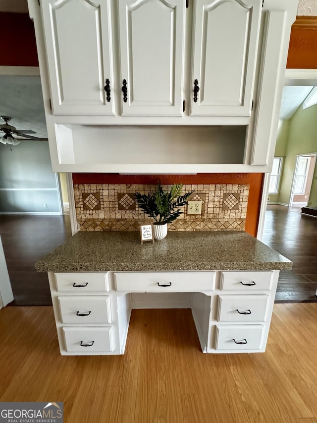 interior details with tasteful backsplash, white cabinetry, built in desk, and light hardwood / wood-style floors